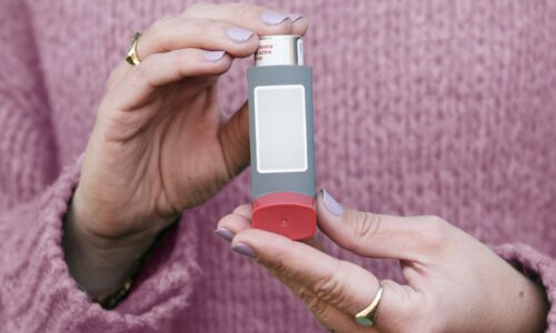 Two hands holding a gray metered-dose inhaler with a blank label in front of a pink knit sweater