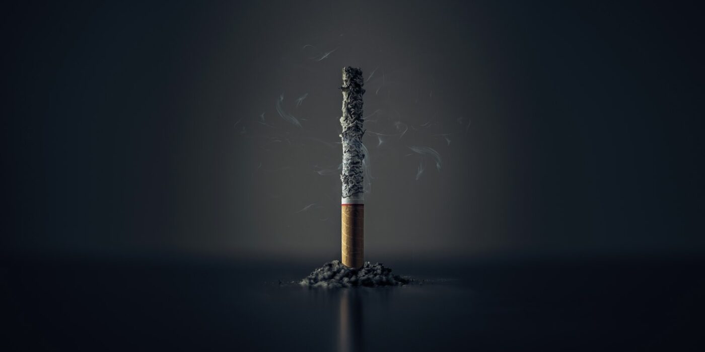A single burnt-down cigarette standing upright in a small pile of ash against a dark background