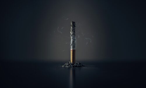 A single burnt-down cigarette standing upright in a small pile of ash against a dark background