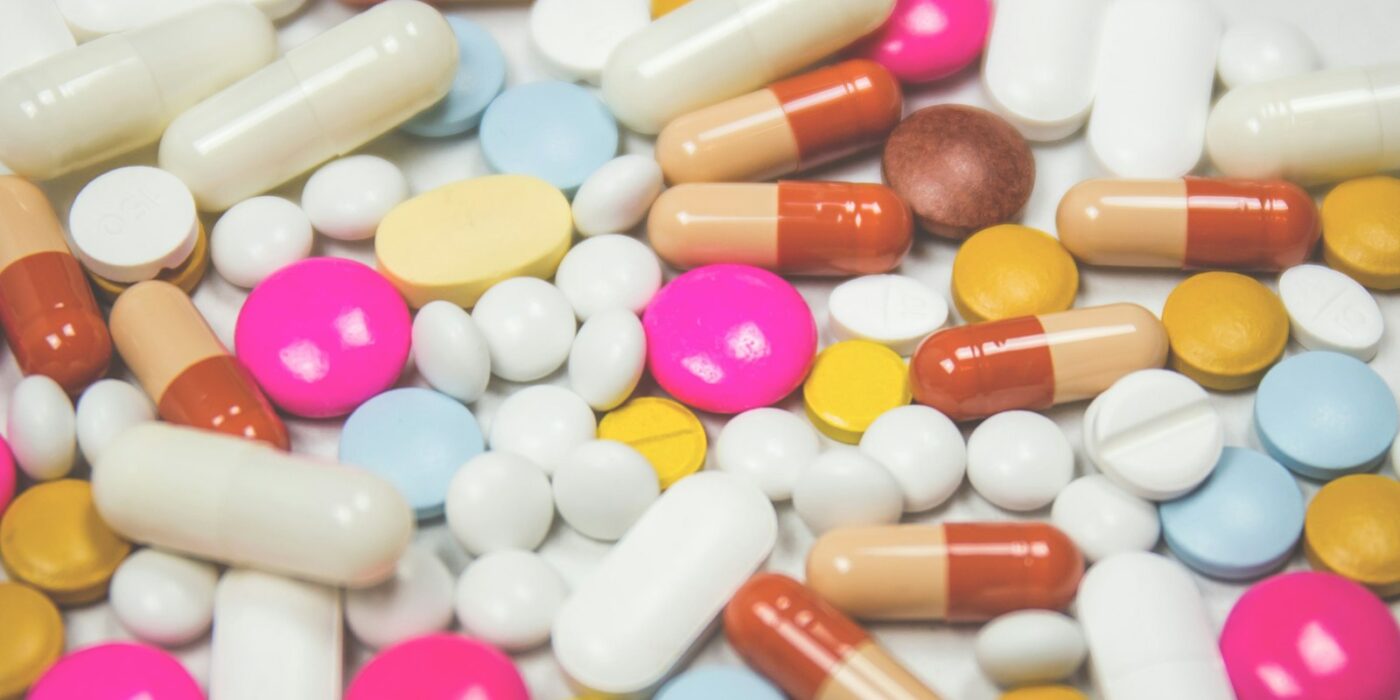 Tablets and capsules in many colors and shapes, including pink, blue, yellow and white pills, on a white surface