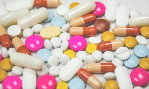 Tablets and capsules in many colors and shapes, including pink, blue, yellow and white pills, on a white surface