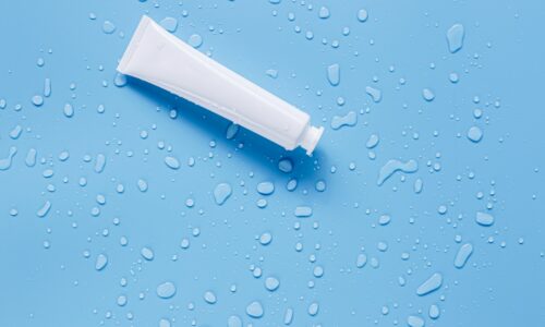 A blank white cream tube lying on a light blue surface scattered with water droplets
